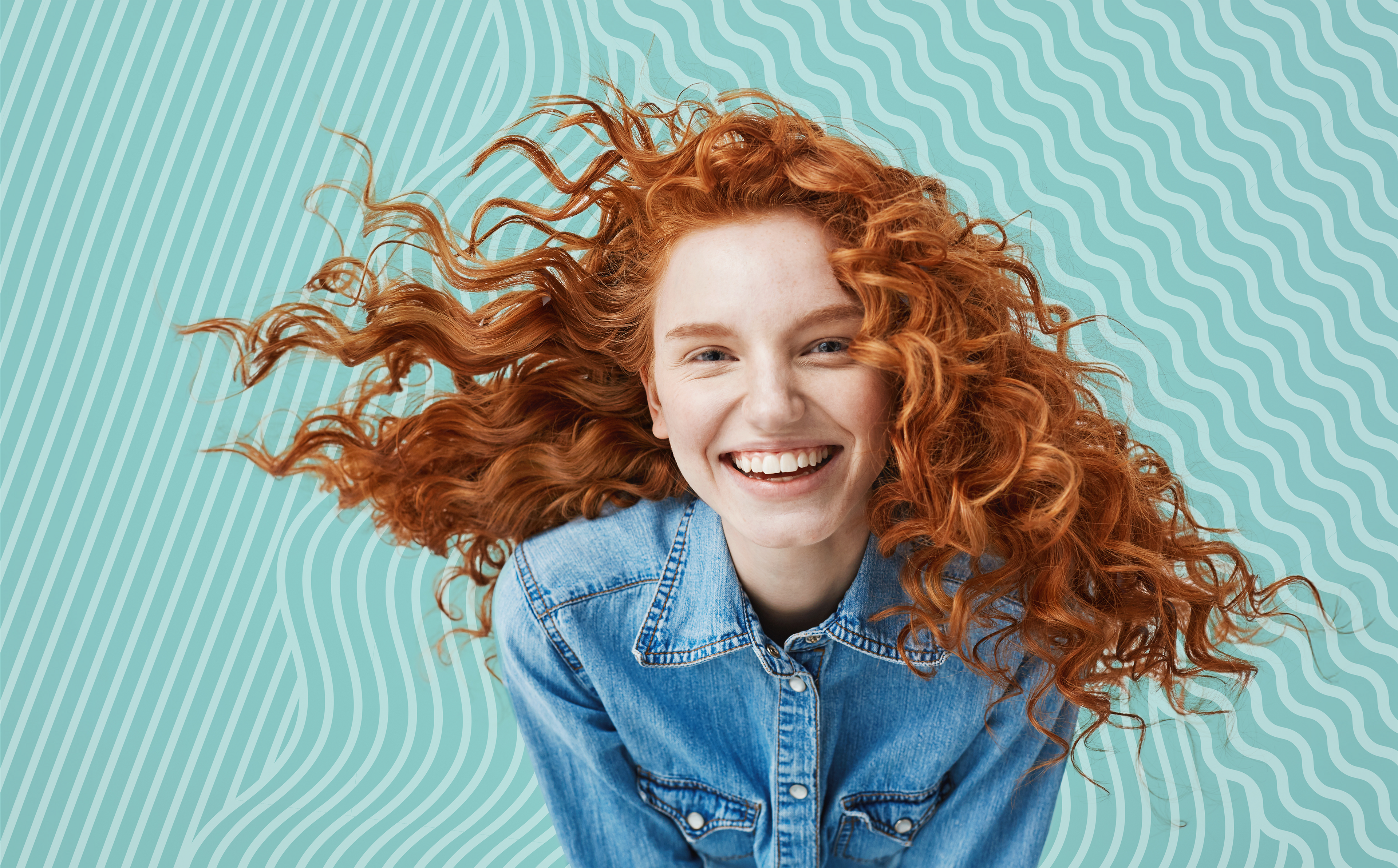 A young woman with curled red hair leans forward, smiling at the camera.
